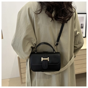 Modella con borsa a tracolla in pelle nera e fibbia a H dorata sopra un cappotto beige