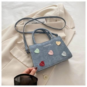 Close-up of blue denim bucket bag featuring colorful heart patches and fashion text detail