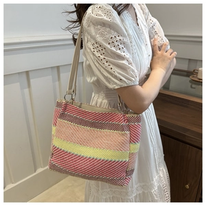 Model wearing multi-colored woven canvas shoulder bag with vibrant stripes and leather straps