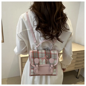 Detail view of pink and green plaid backpack with delicate bow and leather trim