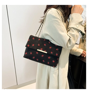 Detail of strawberry print corduroy bag with gold metal clasp and woven chain strap