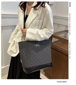 Detail of grey tote bag with heart pattern, white bow, and black leather bottom