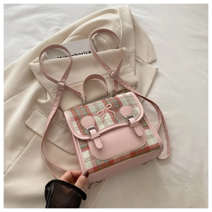 Detail of pink leather and plaid fabric backpack with embroidered bow and buckle straps