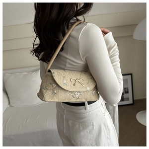 Détail du sac à main en paille beige avec broderie florale et boucle nœud doré