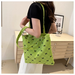 Détail du sac cabas matelassé vert avec imprimés nœuds noirs porté par un mannequin