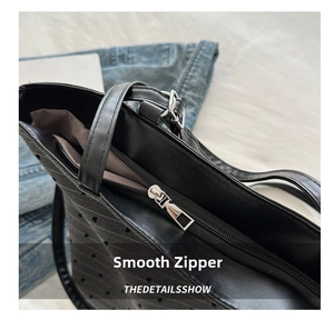 Detailed close-up of smooth silver metal zipper on black textured leather tote bag