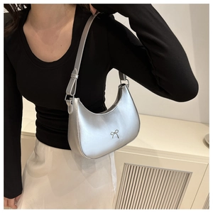 Silver metallic crescent underarm bag with metal bow detail shown on models shoulder