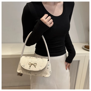 Détail des broderies florales et du nœud doré sur le sac à main en paille beige