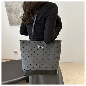 Detail view of large grey tote bag with black polka dots, bow accents and leather base