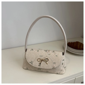 Détail de broderie florale verte et boucle nœud doré sur un sac baguette tissé beige