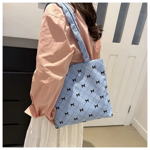 Sac cabas bleu avec motifs de nœuds noirs, porté par un mannequin en intérieur