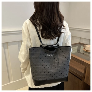 Detail of grey tote with heart texture, metallic bow, and durable leather base on model