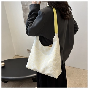 Grand sac fourre-tout tissé beige avec anses en cuir jaune porté à l'épaule par un mannequin
