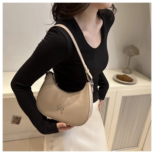 Detail shot of a beige half-moon shoulder bag with a silver metal bow decoration