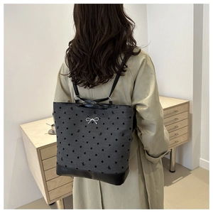 Detail of grey polka dot tote with bow accents on model in elegant beige coat