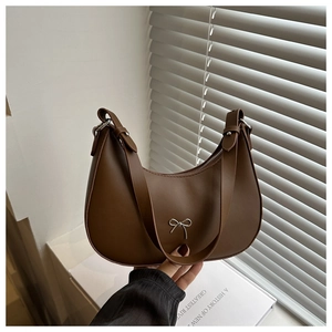 Brown half-moon leather underarm bag with silver bow accent shown in hand
