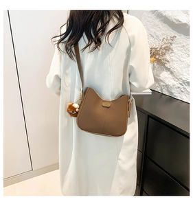 Detail of a brown leather hobo bag with gold metal plate and brown plush ball charm