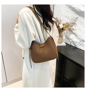 Detail of a brown leather bucket bag with fashion metal plate on a white coat model
