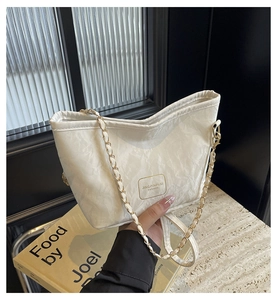 Detail of white textured bucket bag with gold logo plaque and woven chain strap