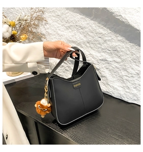 Detail of a matte black bucket bag featuring gold 'FASHION' lettering and a plush charm