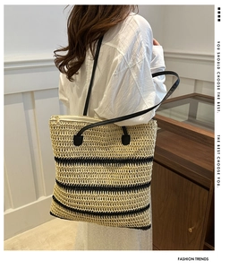 Detail of woven straw tote bag with black stripes and leather straps worn by model