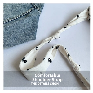 Detail view of white fabric shoulder strap featuring black bow patterns and knotted design