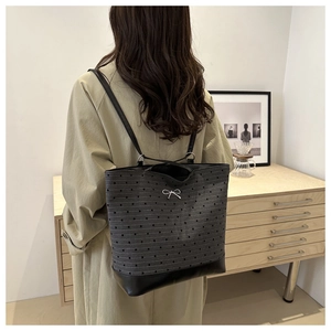 Detail of grey canvas tote with heart patterns, leather base, and silver bow accent