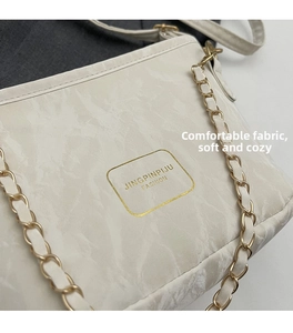 Detail of off-white bucket bag featuring marble texture and gold chain strap accents