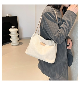 Detail of minimalist beige corduroy tote bag featuring a brown leather logo patch and slim straps