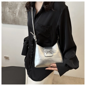 Close-up of a silver metallic shoulder bag featuring a stylish metal bow and knotted strap