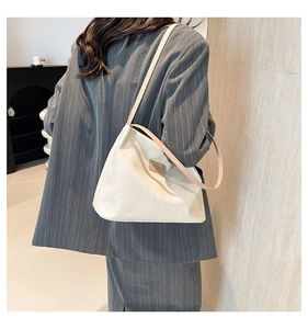 Detail of white textured fabric shoulder bag with leather logo patch on striped blazer
