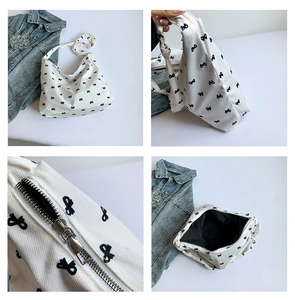 Detail view of white canvas shoulder bag with black bow prints and metal zipper closure