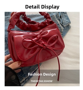 Detail of red glossy patent leather handbag featuring bow pleats and scrunchie handle
