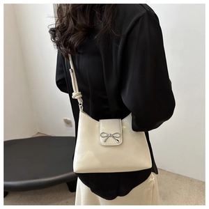 Detail of a creamy white shoulder bag with a silver metallic bow and smooth finish