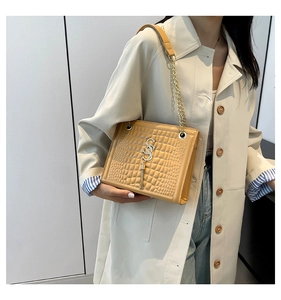 Détail du sac bandoulière beige avec texture crocodile et breloque à pompon doré