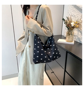Detail of a black tote bag with white bow patterns worn by a model in a minimal setting