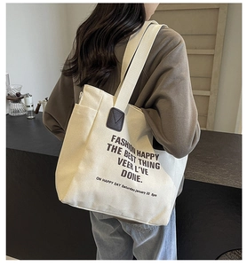 Detail of off-white canvas tote bag featuring bold black slogan and leather handle accents