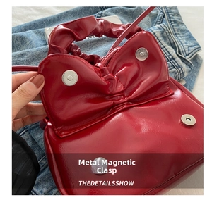 Detail of the double magnetic snap closure on a red glossy bow-shaped shoulder bag