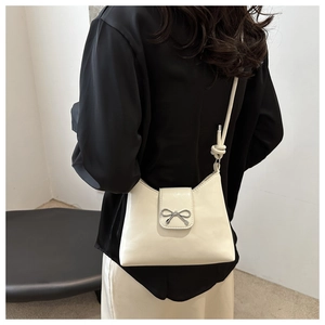 Detail of cream leather bucket bag with silver bow buckle and knotted strap on model