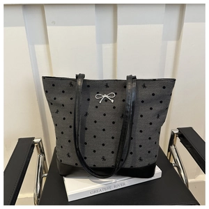 Polka dot fabric tote bag with bow detail and black faux leather base on a chair