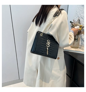 Détail du sac noir à texture crocodile avec boucle S dorée et pompon sur un manteau blanc