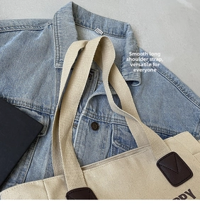 Detail of beige canvas tote bag showing wide woven shoulder strap and brown leather accents