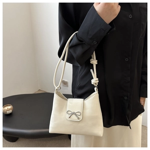 Detail of cream white shoulder bag featuring a silver metal bow and knotted rope strap