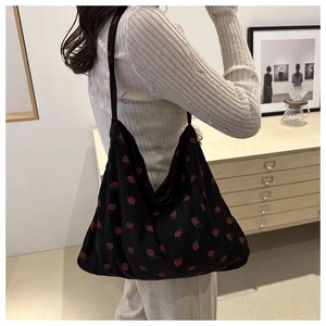 Gros plan du sac cabas en velours noir à motifs fraises porté par un mannequin