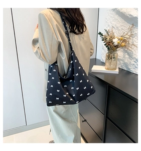Close-up of large black tote bag with white bow prints and wide shoulder strap