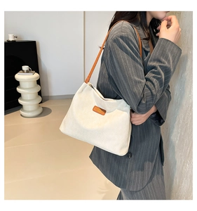 Close-up of white textured fabric shoulder bag with brown leather strap and logo detail