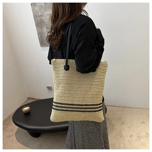 Detail of hand-woven straw tote bag featuring a black striped base and thin shoulder straps