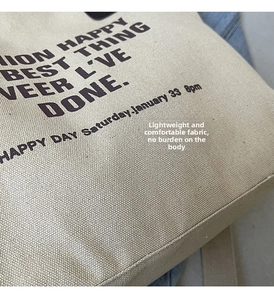 Detail shot of the reinforced stitching and black serif lettering on beige canvas tote bag