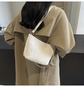 Detail of white marble textured tote bag with golden chain strap on a trench coat