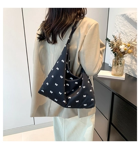 Detail of black canvas tote bag with white bow patterns worn by a model in a casual setting